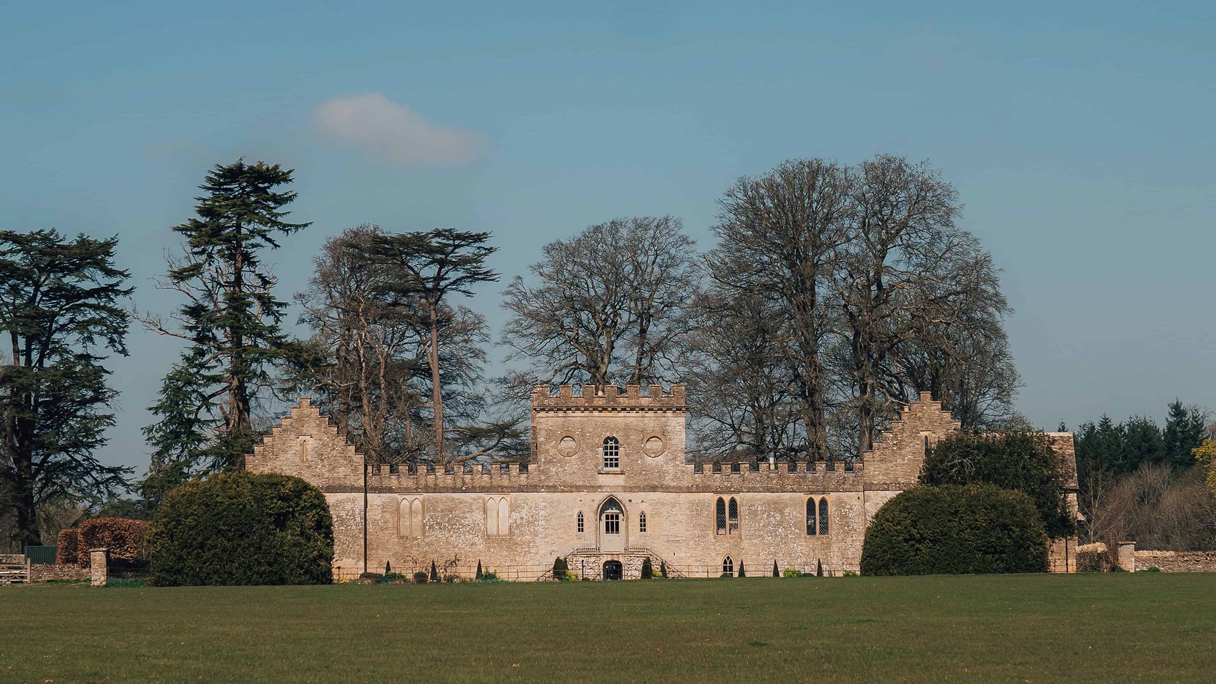 Ivy Lodge full exterior view of castellated Grade II listed building across parkland, Cirencester Park